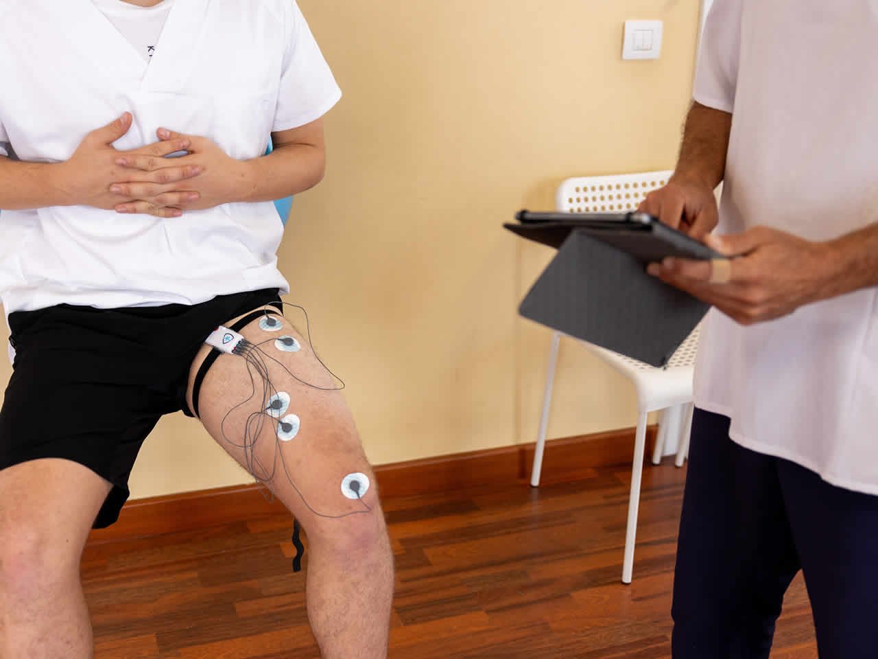 FISIOTERAPEUTA MANEJANDO UNA MAQUINA DE ELECTROESTIMULACION EN EL MUSLO DE UN PACIENTE